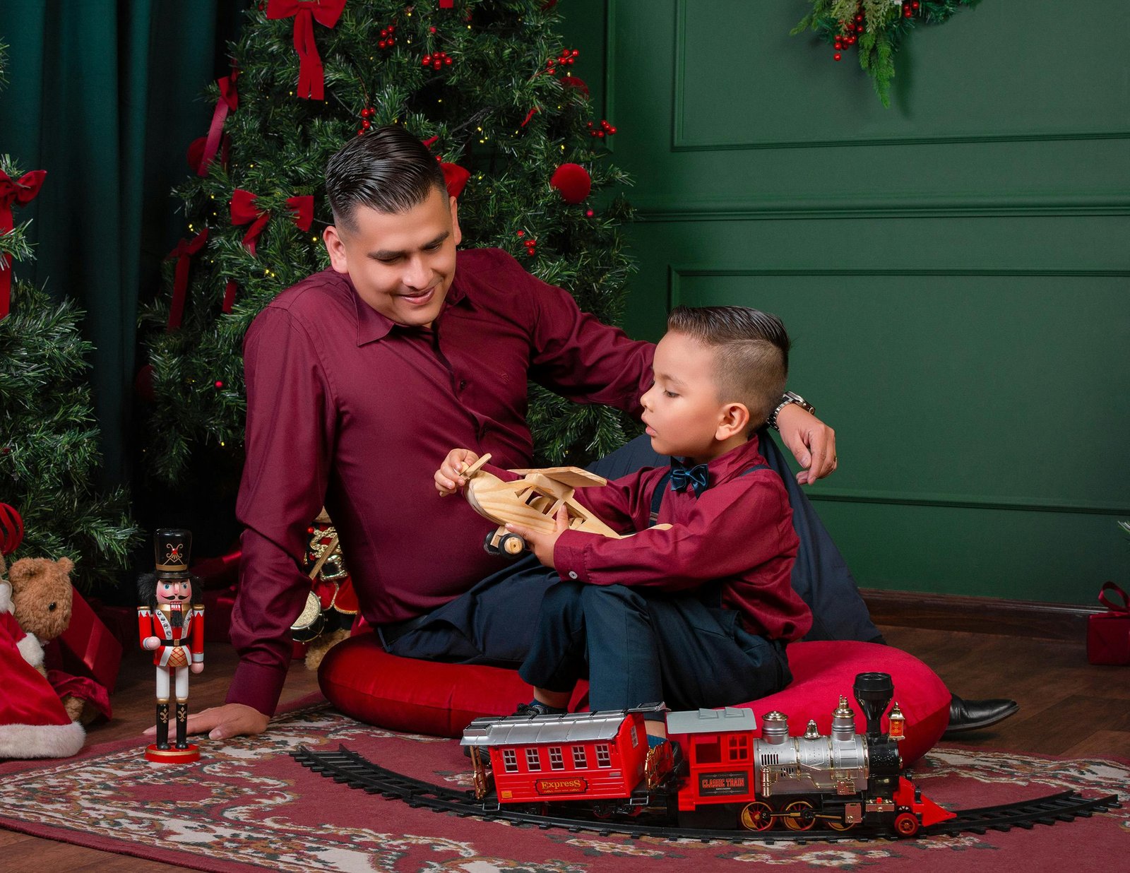 A father and son enjoy Christmas at home, playing with toys by the decorated tree.