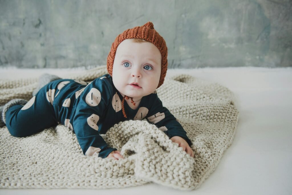 Cute baby in cozy knitted outfit lying on a soft blanket indoors.