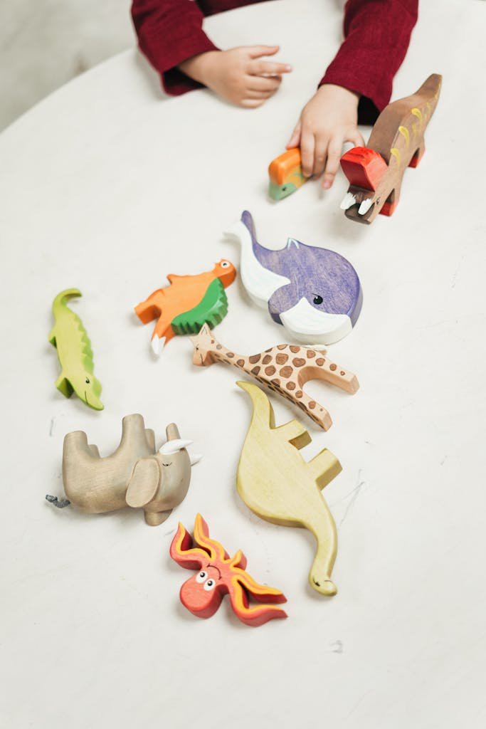 A child plays with a variety of colorful wooden animal toys on a white table indoors.