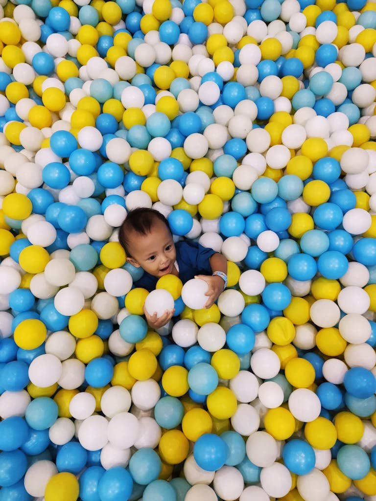 A happy baby playing in a vibrant ball pit, surrounded by colorful balls in Indonesia.