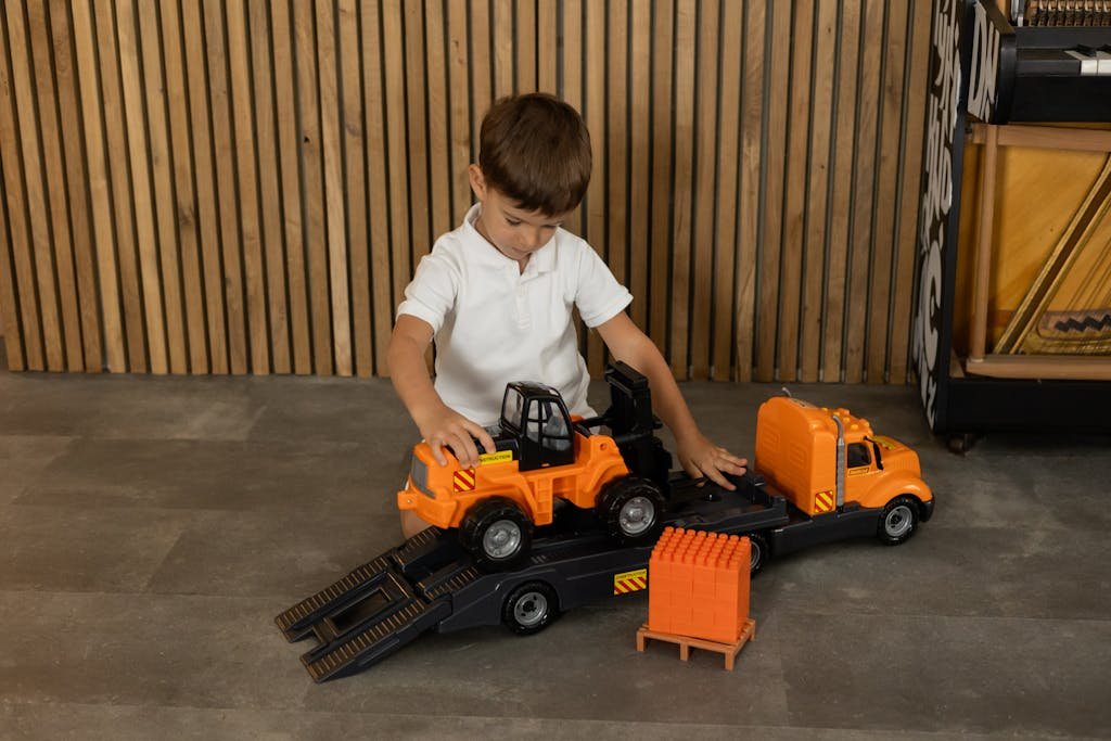A young boy plays inside with a construction-themed toy truck and car, creating imaginative scenarios.