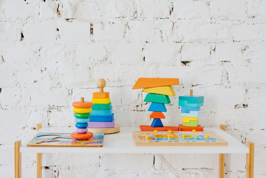 Vibrant wooden stacking toys displayed on a minimalist white table against a white brick wall.